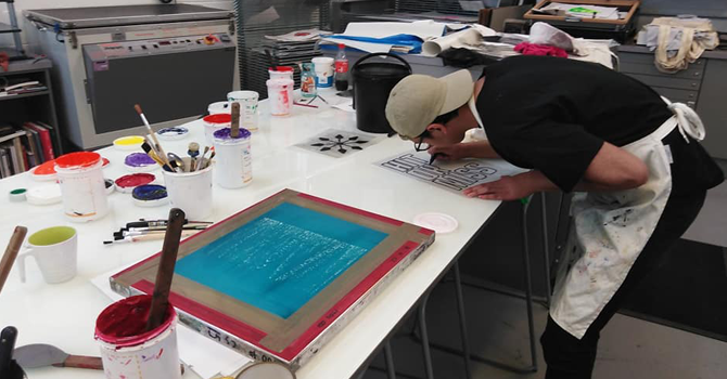 a man leabing over a desk at a screen printing workshop