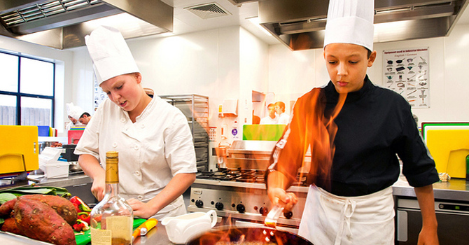 Two students cutting and drying food with chefs hats on