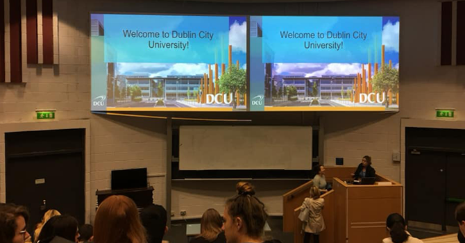 Screens in a lecture theatre which read "Welcome to Dublin City University"