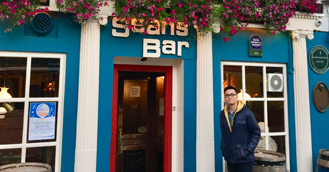 Student stands in front of the facade of Sean's bar with flowers hanging overhead