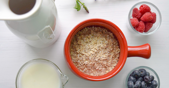 porridge in a red bowl with a jug of milk and some fruit beside it