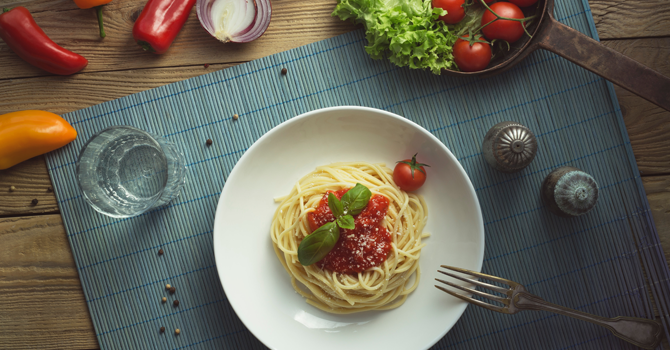 A plate of spaghetti with tomato sauce on top and vegetables on the table around it