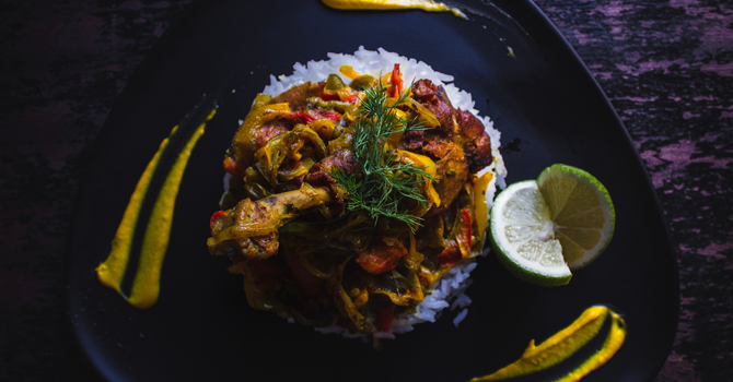 A dish with a pile of rice as well as spiced meat and vegetables