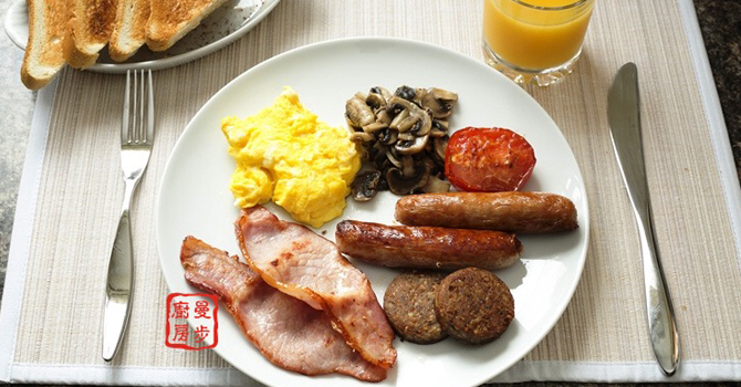 A plate filled with scrambles eggs, sausages, bacon, mushrooms and pudding