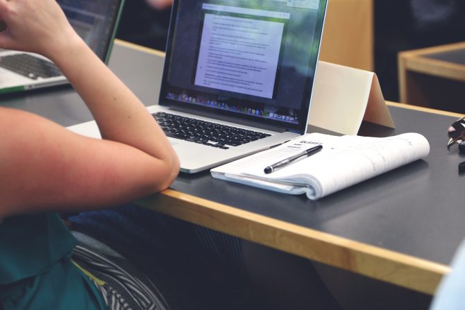 Person siting in lecture hall with laptop taking notes