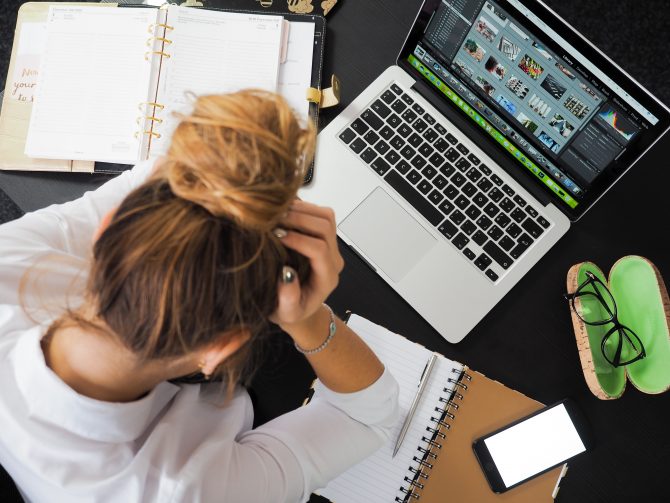 Woman stressed sitting at a desk witha laptop, books and a smartphone