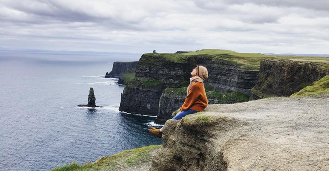 A girl sits on the cliff edge at the Cliffs of Moher