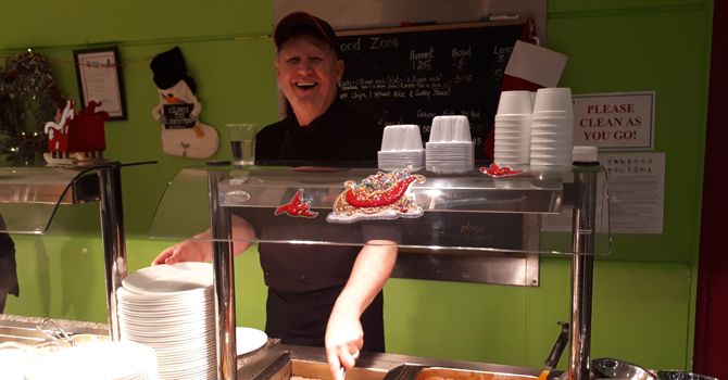 A smiling man serves lunch in a university cafeteria