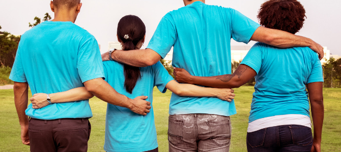 Group of four peopole in blue t shirts with arms interlinked.