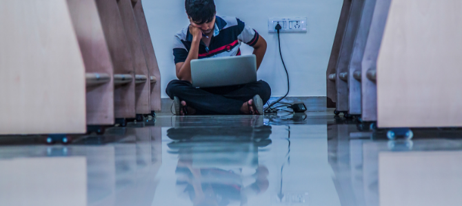 male student sitting on floor of library charging a laptop