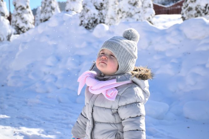 small child standing in snow wearing hat and scarf