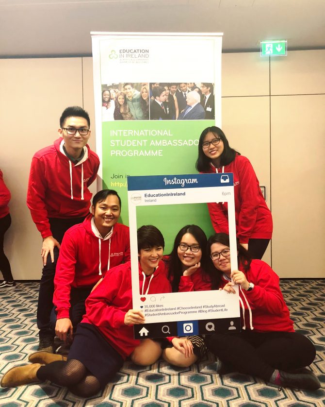 Group of students in matching red hoodies posing with a mock instagram photo frame 