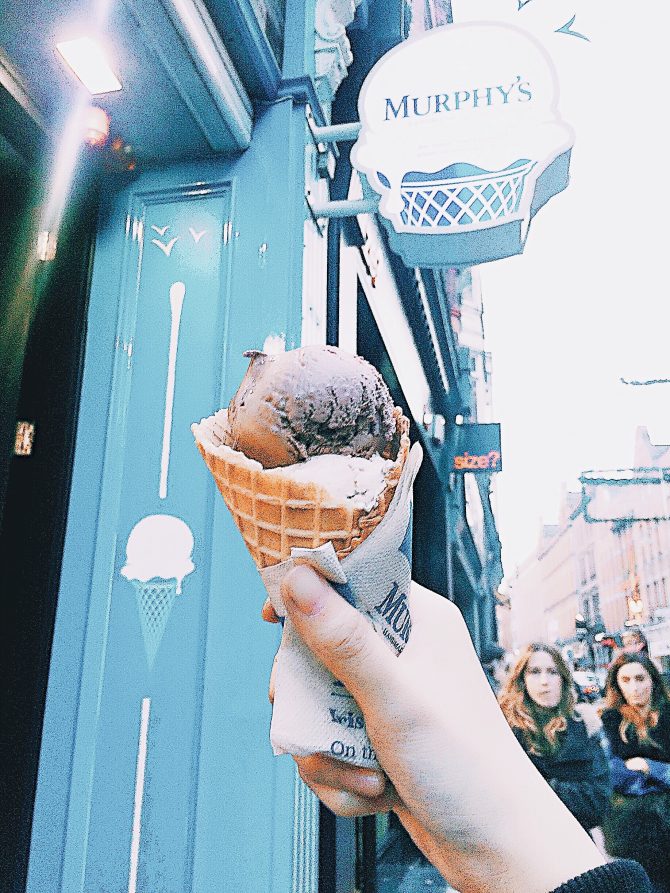 hand holding a chocolate and vanilla ice cream cone outside a blue painted shop front 