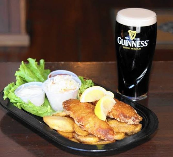 Fish and chips with lemon wedgews and tartare sauce next to a pint of Guinness 
