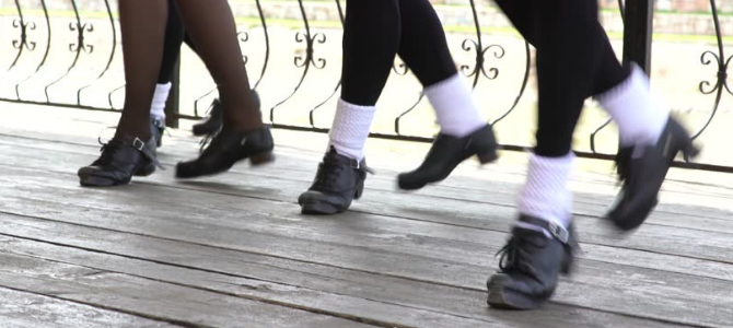 three sets of feet in Irish dancing shoes dancing on a wooden floor