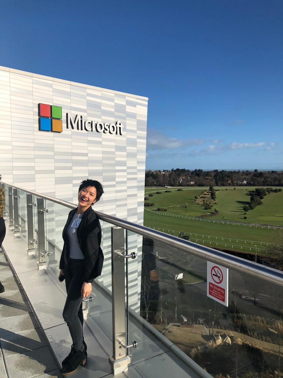 smiling woman in front of Microsoft building with blue sky and green fields in the background 
