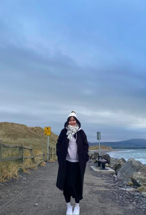 Picture of a girl dressed in warm clothes standing on a low laying road beside the sea