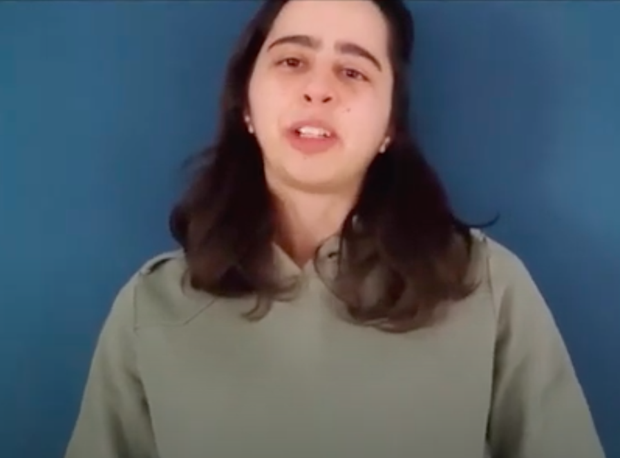 A screenshot from a video showing Bruna in front of a dark blue wall